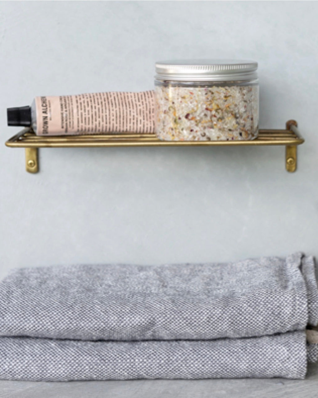 Simple brass wire shelf with jar of bath salts and salve resting on top